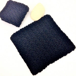 May include: Two black crocheted dishcloths, one larger than the other, on a white surface.