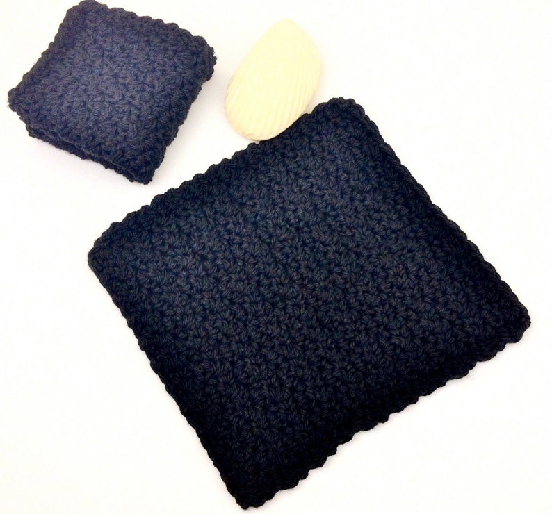 May include: Two black crocheted dishcloths, one larger than the other, on a white surface.