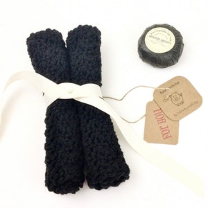 May include: Two black crocheted dishcloths tied together with a white ribbon and a brown gift tag that says "FOR YOU!" with a small pig illustration and the text "hand crocheted" in red. A round black soap bar with a white label that says "Pure Vegetable Oil Soap MOLTON BROWN 50g/1.75oz" is also included.