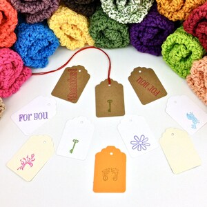 May include: A variety of colorful crocheted rolls with brown, white, and orange gift tags. The tags have different designs and text, including "For You", "Thanks!" and "For You".