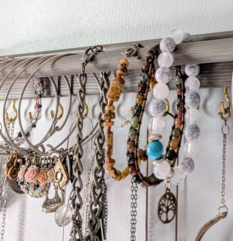 Puede incluir: Una exhibici&oacute;n de varios collares y pulseras. La joyer&iacute;a incluye cadenas de plata, pulseras de cuentas con cuentas turquesas y marmoladas, y collares con colgantes florales y geom&eacute;tricos. La joyer&iacute;a cuelga de un estante de madera.