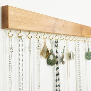 May include: A wooden jewelry organizer with multiple hooks for hanging necklaces and earrings. The organizer is made of light brown wood and has a natural finish.
