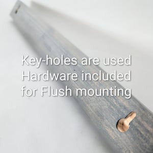 Puede incluir: Primer plano de un marco de madera gris con agujeros para llaves y una clavija de madera. El texto en el marco dice: "Los agujeros para llaves se utilizan, Hardware incluido para montaje empotrado."