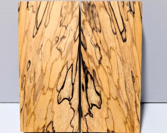 Puede incluir: Dos bloques rectangulares de madera veteada con un color base bronceado claro, con prominentes líneas orgánicas negras y patrones intrincados que recorren toda la veta, dispuestos uno al lado del otro verticalmente.
