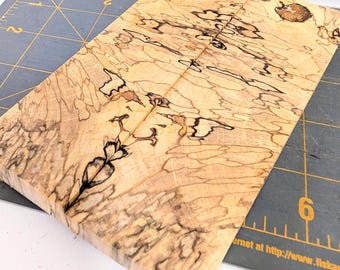 Puede incluir: Dos piezas rectangulares de madera de arce veteado con un color base bronceado claro y patrones de líneas negras intrincadas. La madera está colocada sobre una alfombrilla de corte gris oscuro con líneas de cuadrícula y números amarillos.