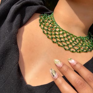 May include: A choker necklace crafted from small, translucent green beads arranged in a delicate, interconnected net pattern. The necklace sits closely around the neck, featuring a repeating diamond-shaped mesh structure made of individual green beads.