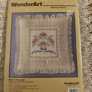 Könnte beinhalten: Ein WonderArt Stickkissen-Set mit einem gestanzten Design eines Blumenstraußes mit Schleife. Die fertige Größe des Kissens beträgt 35,56 x 35,56 cm. Das Set enthält 100% Baumwollstoff, Wollgarn, Baumwoll-Stickgarn, Ösenspitze, eine Sticknadel und Anleitungen. Das Set enthält keine Kissenfüllung. Hergestellt und gedruckt in den USA.
