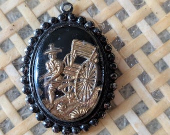 Peut inclure: Pendentif ovale avec un fond noir et une scène de calèche dorée. Le pendentif est encadré d'une bordure perlée noire et comporte une petite boucle en haut pour l'accrocher. La scène de la calèche représente une personne tirant une calèche.