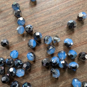 May include: A collection of blue and iridescent glass beads, some with a frosted finish, scattered on a wooden surface.
