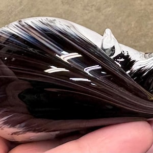 Puede incluir: Una figura de vidrio soplado a mano, lisa, con forma de gato enroscado. La pieza presenta un núcleo negro profundo que se transforma en vidrio transparente translúcido en los bordes, con delicados mechones blancos que se arremolinan.