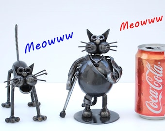 May include: Two metal cat sculptures with the word "Meowww" in blue and red. The cat sculptures are made of metal and have a unique, industrial design. A Coca-Cola can is next to the cat sculptures.