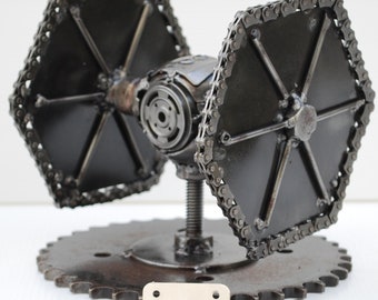 May include: A black metal TIE fighter model made from recycled materials. The model is on a circular base and includes extra parts, such as screws and nuts.