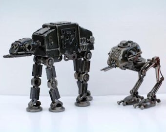 May include: Two metal model AT-AT walkers from Star Wars, one larger than the other, next to a can of Coca-Cola.