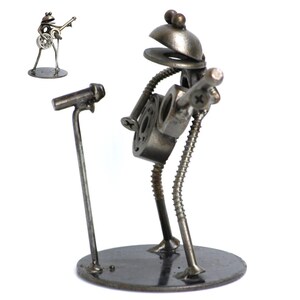May include: A metal sculpture of a frog playing a guitar, with a microphone stand in front. The frog is made of nuts, bolts, and washers, with a round base. A smaller version of the sculpture is in the upper left corner.