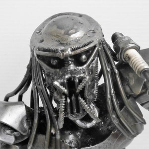 May include: A metal sculpture of a Predator, a fictional alien hunter, made from recycled materials. The sculpture is detailed and realistic, with a menacing expression.