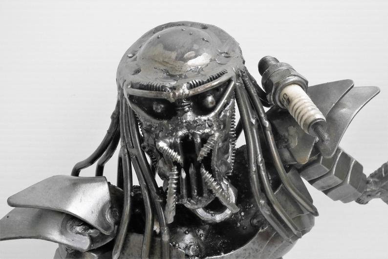 May include: A metal sculpture of a Predator, a fictional alien hunter, made from recycled materials. The sculpture is detailed and realistic, with a menacing expression.
