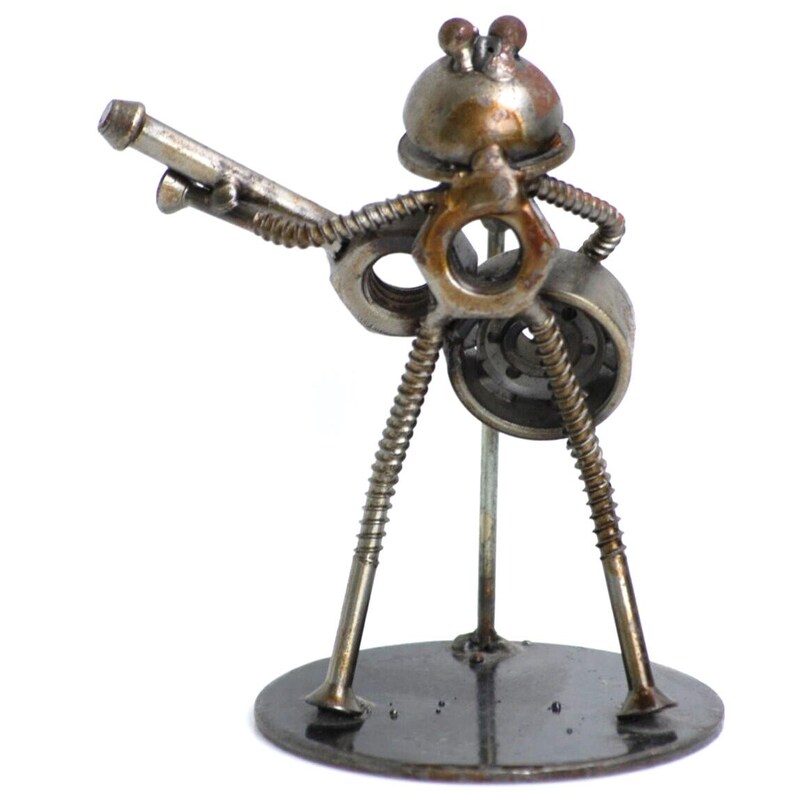 May include: A handcrafted metal sculpture of a musician playing a guitar. The figure is constructed from nuts, bolts, screws, and other hardware, with a round base. The sculpture has a rustic, industrial aesthetic.