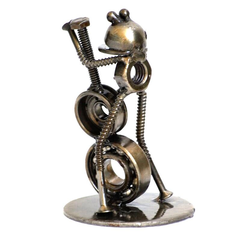 May include: A whimsical metal sculpture of a frog playing a guitar. The frog is crafted from nuts, bolts, and bearings, with a round base. The sculpture has a metallic bronze finish and is set against a white background.