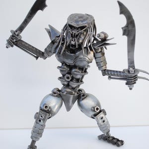 May include: A silver Predator action figure made of metal parts, such as nuts, bolts, and gears. The figure is holding two swords and has a menacing expression.
