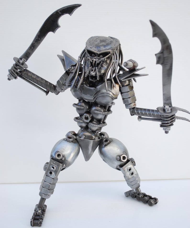 May include: A silver Predator action figure made of metal parts, such as nuts, bolts, and gears. The figure is holding two swords and has a menacing expression.