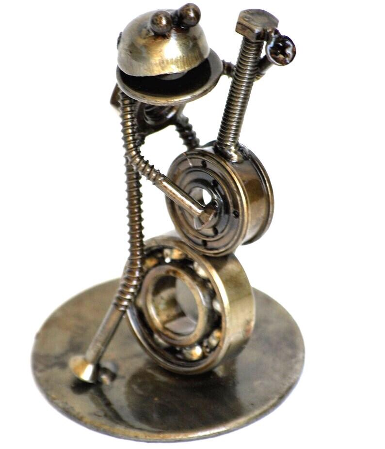May include: A whimsical sculpture of a frog playing a banjo, crafted from repurposed metal hardware. The frog's head is a rounded piece, with a body made of a spring and screws. The banjo is made from a bearing and other metal parts, all mounted on a circular base.