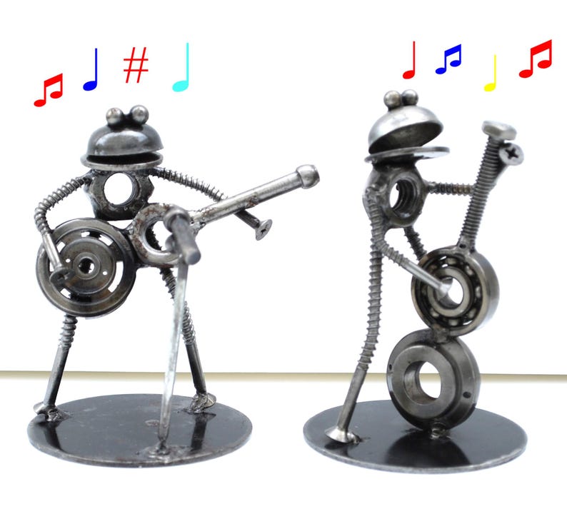 May include: Two metal frog sculptures playing musical instruments. One frog plays a guitar, the other a bass. Both are made from nuts, bolts, and washers. Colorful musical notes are above the sculptures.