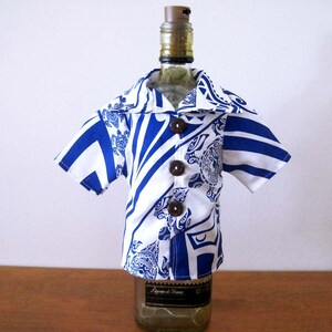 May include: A short-sleeved button-down shirt cover for a bottle, featuring a white and blue geometric and floral pattern. The garment has a wide collar and three dark brown circular buttons down the front, fitted over a glass bottle.