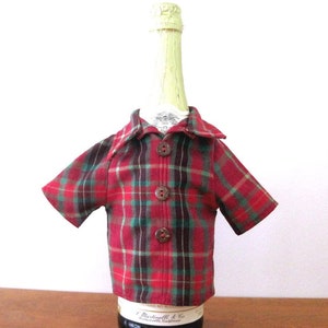 May include: A red and green plaid shirt bottle cover with brown buttons. The shirt is made of fabric and has short sleeves. The bottle cover is designed to fit a standard-sized bottle of wine or champagne.