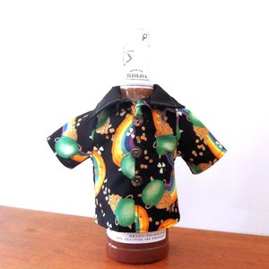May include: A black shirt with a green, gold, and rainbow pattern of shamrocks and pots of gold. The shirt is being used as a bottle cover for a brown glass bottle.