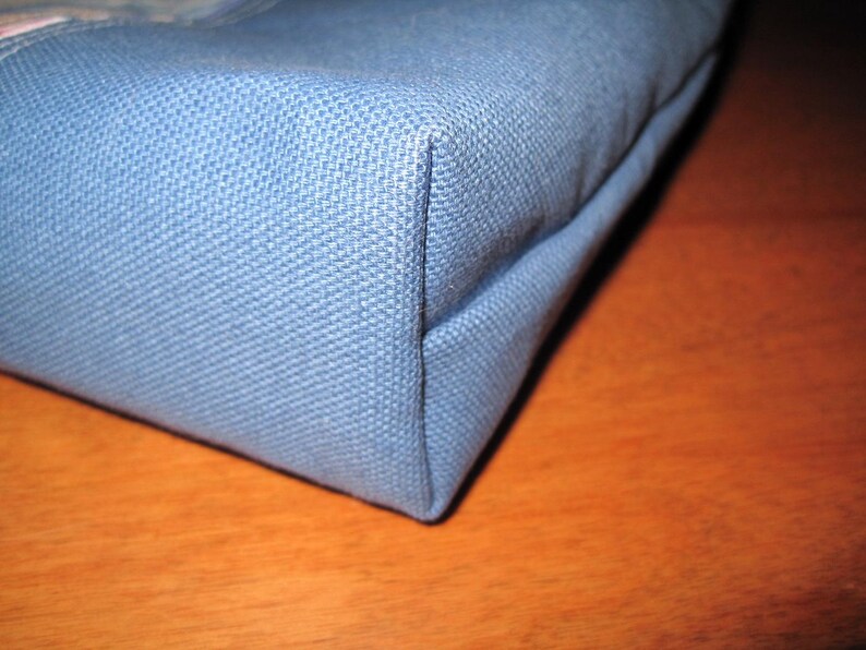 Puede incluir: Primer plano de una esquina de una bolsa de tela azul claro. La bolsa tiene un tejido texturizado y est&aacute; construida con costuras precisas. La esquina est&aacute; bien definida, mostrando la forma y la construcci&oacute;n de la bolsa. La bolsa es probablemente un bolso tote o similar.