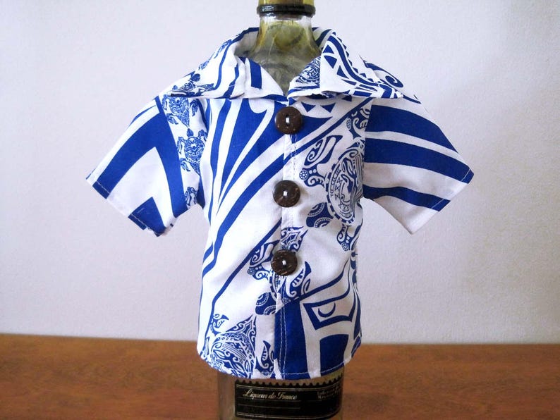 May include: A short-sleeved button-down shirt featuring a white and blue patterned design with sea turtle motifs. The garment has a wide collar and three dark brown circular buttons down the front, fitted over a glass bottle.