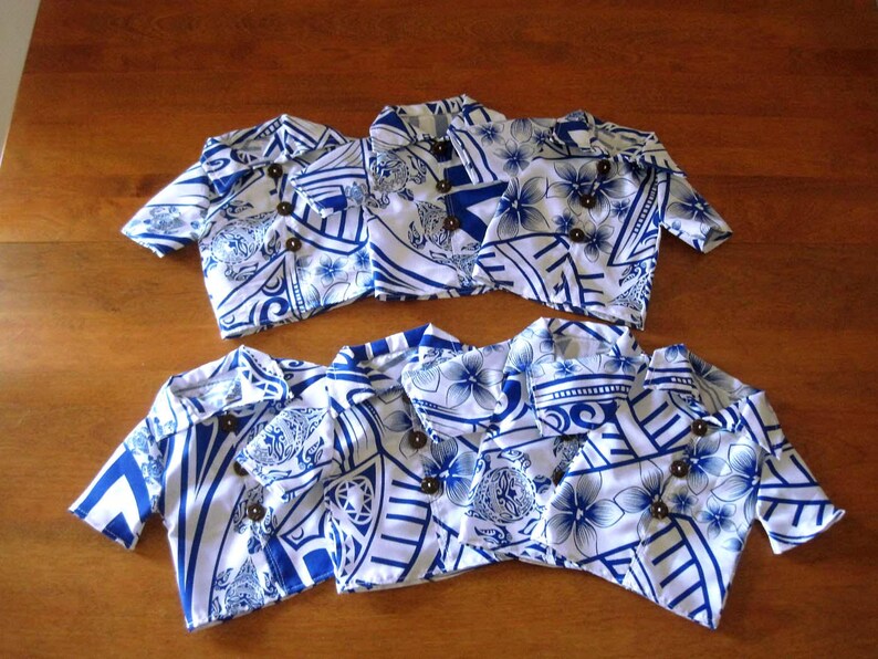 May include: Six short-sleeved button-down shirts featuring a white and blue floral and geometric pattern. Each shirt has a pointed collar and three dark brown circular buttons down the front. The shirts are arranged in two rows of three on a surface.