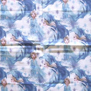 Puede incluir: Patr&oacute;n repetido con un personaje de dibujos animados con un vestido azul claro y pelo rubio largo. El dise&ntilde;o incluye elementos azules y blancos arremolinados y acentos de copo de nieve. El tema general es un motivo de invierno o fantas&iacute;a.