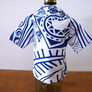May include: A short-sleeved shirt cover for a bottle featuring a white base with a bold blue graphic pattern. The garment has a collared neckline and a button-down front design, fitted over the neck and upper body of a glass bottle.