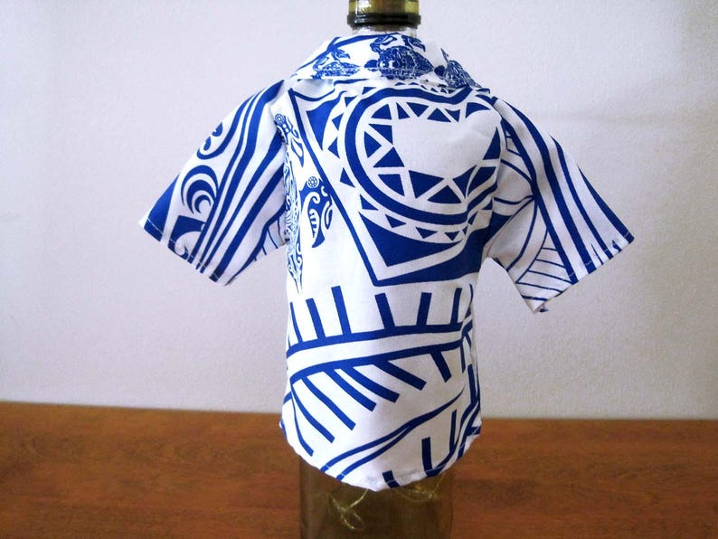 May include: A short-sleeved shirt cover for a bottle featuring a white base with a bold blue graphic pattern. The garment has a collared neckline and a button-down front design, fitted over the neck and upper body of a glass bottle.