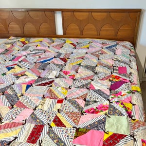May include: A colorful patchwork quilt with a variety of fabric patterns, including stripes, florals, and solid colors. The quilt is spread across a bed with a wooden headboard. The quilt's design features triangles and squares.