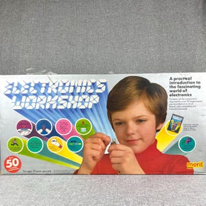 May include: Electronics Workshop box set with a young person holding components. The box features the text "ELECTRONICS WORKSHOP" in blue and white, with colorful illustrations and the text "50 exciting experiments". The box also includes the text "For ages 10 years upwards".