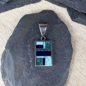 May include: A rectangular silver pendant featuring an inlaid mosaic design. The inlay consists of dark blue lapis lazuli, green turquoise with black matrix, and iridescent white opal segments arranged in a geometric pattern with a silver bail.