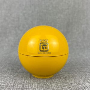 May include: A bright yellow, spherical container with the word "KIKU" and a logo printed on the front. The text "BATH POWDER" is printed below the logo. The container is likely for bath products.