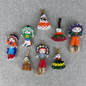May include: A collection of eight handcrafted ornaments made from small, colorful glass beads. Each ornament features a unique figure or shape, including stylized dolls with beaded clothing, hats, and fringe details, all suspended by small leather loops.