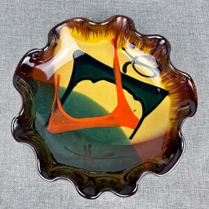 May include: A ceramic bowl with a scalloped edge and an abstract design in shades of brown, yellow, orange, green, and black.