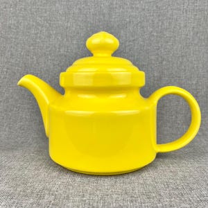 May include: A bright yellow ceramic teapot with a rounded body and a lid with a knob on top. The teapot has a spout on one side and a handle on the other.