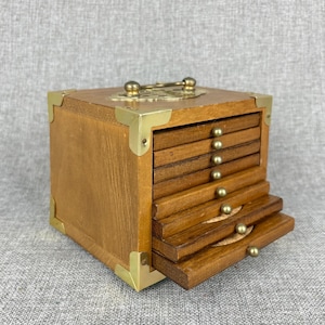 May include: A wooden coaster set with a square box. The box has brass corner protectors and a brass handle. The coasters are made of wood and have brass knobs. The set is designed to hold multiple coasters.