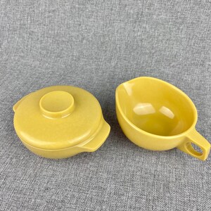 May include: A set of two yellow ceramic bowls. One bowl has a lid and the other has a handle.