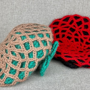 May include: Close-up of two handmade crochet items. One is a tan and teal mitten with a lattice design. The other is a red and black openwork hat. Both items are on a gray surface.