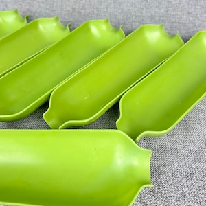 May include: Five green plastic serving dishes, shaped like long, narrow bowls, are stacked on top of each other. The dishes are made of a smooth, glossy plastic.