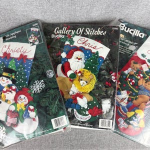 May include: Three Bucilla felt appliqué Christmas stocking kits. One features a snowman, the second Santa Claus and a lion, and the third has teddy bears. The kits are in plastic packaging.