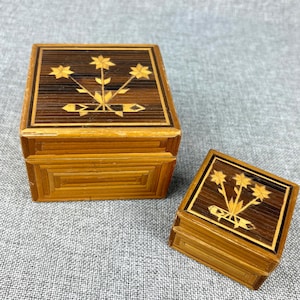 May include: Two wooden boxes with intricate floral designs made from thin strips of wood. The larger box is brown with a light brown floral design and the smaller box is light brown with a dark brown floral design.
