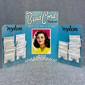 May include: A blue and white cardboard display card for Bead Cord nylon thread. The card features a photo of a woman with a beaded necklace and the text "Bead Cord - Needle-and - Twisted Needle Woven in the Cord". The card has samples of different sizes of nylon thread.