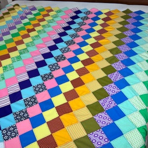 May include: A colorful patchwork quilt with a variety of patterns and colors, including pink, blue, green, yellow, and brown. The quilt is made of squares sewn together in a diagonal pattern.